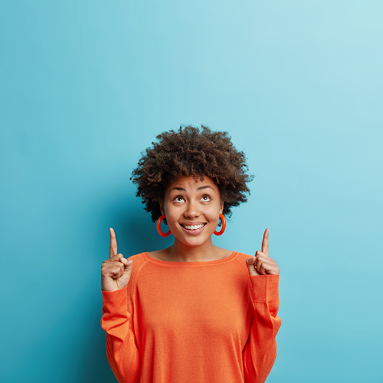 We have a woman with brown frizzy hair pointing her index fingers up. The background of the image is light blue.